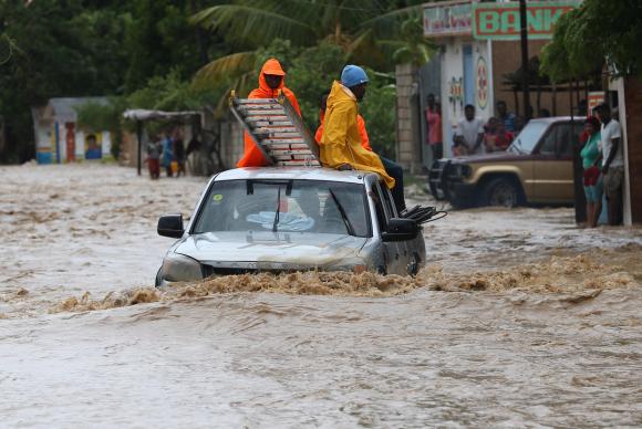 Um grupo de pessoas tenta cruzar uma via alagada in Leogane, no Haiti, após a passagem do Furacão Matthew. O país já registrou 21 mortes em decorrência do furacão (Foto: Orlando Barria/EPA/Agência Lusa/direitos reservados)