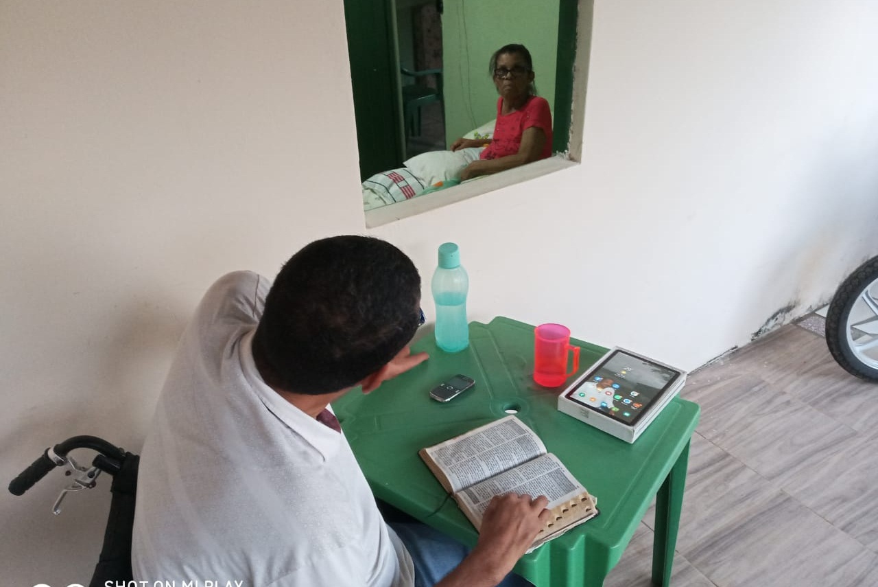 ‘(...)ou seja, que Deus em Cristo estava reconciliando consigo o mundo, não lançando em conta os pecados dos homens, e nos confiou a mensagem da reconciliação’. (2 Coríntios 5:19). Franco lendo a Bíblia para a sogra, dias antes de ela falecer. Foto: Jaqueline Cardoso