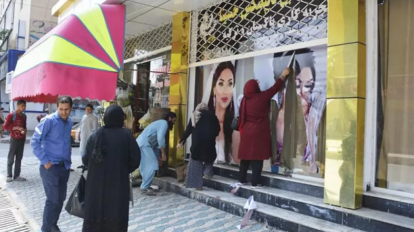 Trabalhadores em um salão de beleza cobrem grandes fotos de mulheres em parede em Cabul, em 15 de agosto de 2021 (Foto: Kyodo News/Getty Images)