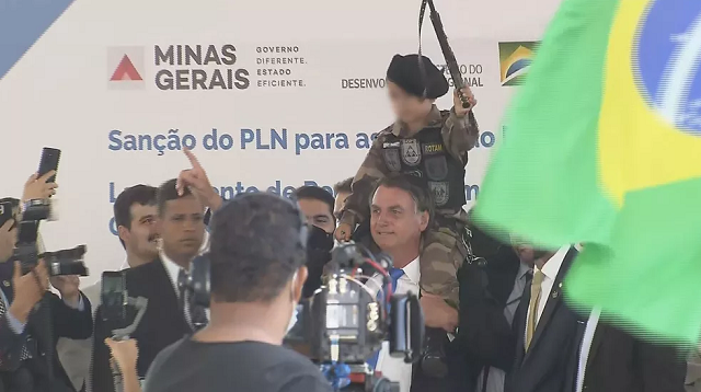 Bolsonaro posa para fotos com criança fardada e com arma de brinquedo na mão, em evento de BH (Foto: TV Globo)
